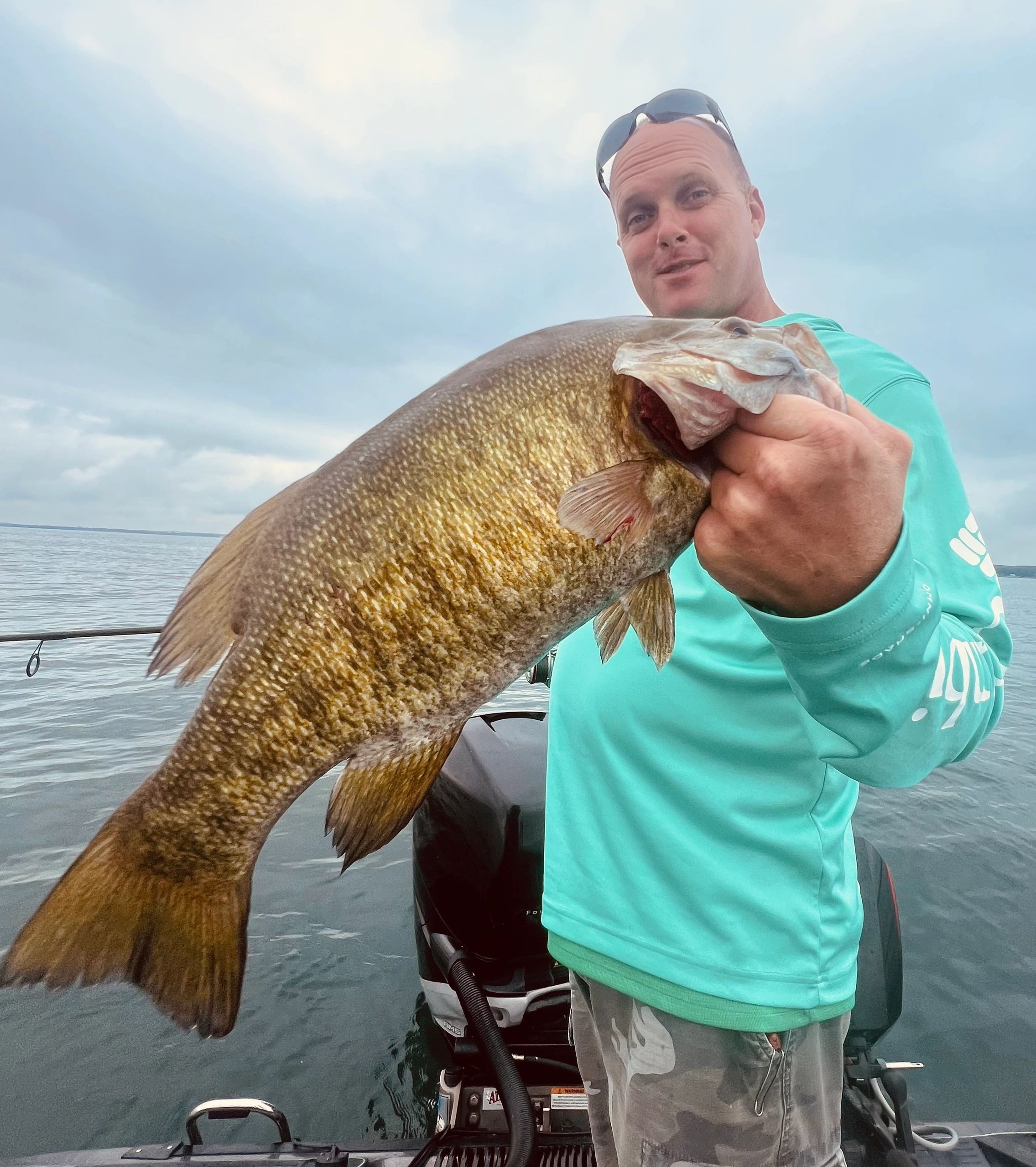 Man holding a large fish on a boat with cloudy sky.