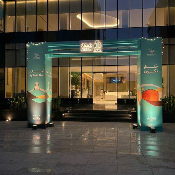 Illuminated entrance archway labeled 'MODON' in front of a modern glass building at night.