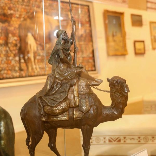 Bronze sculpture of a man riding a camel, holding a spear.