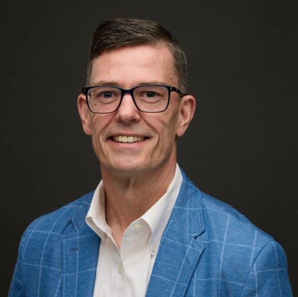 Smiling man wearing glasses and a blue checkered blazer.