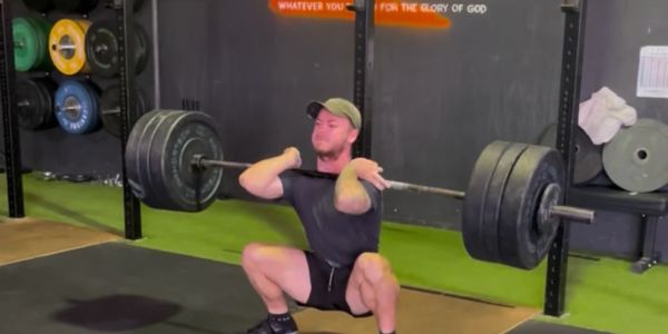 Man doing a front squat with heavy weights in gym.