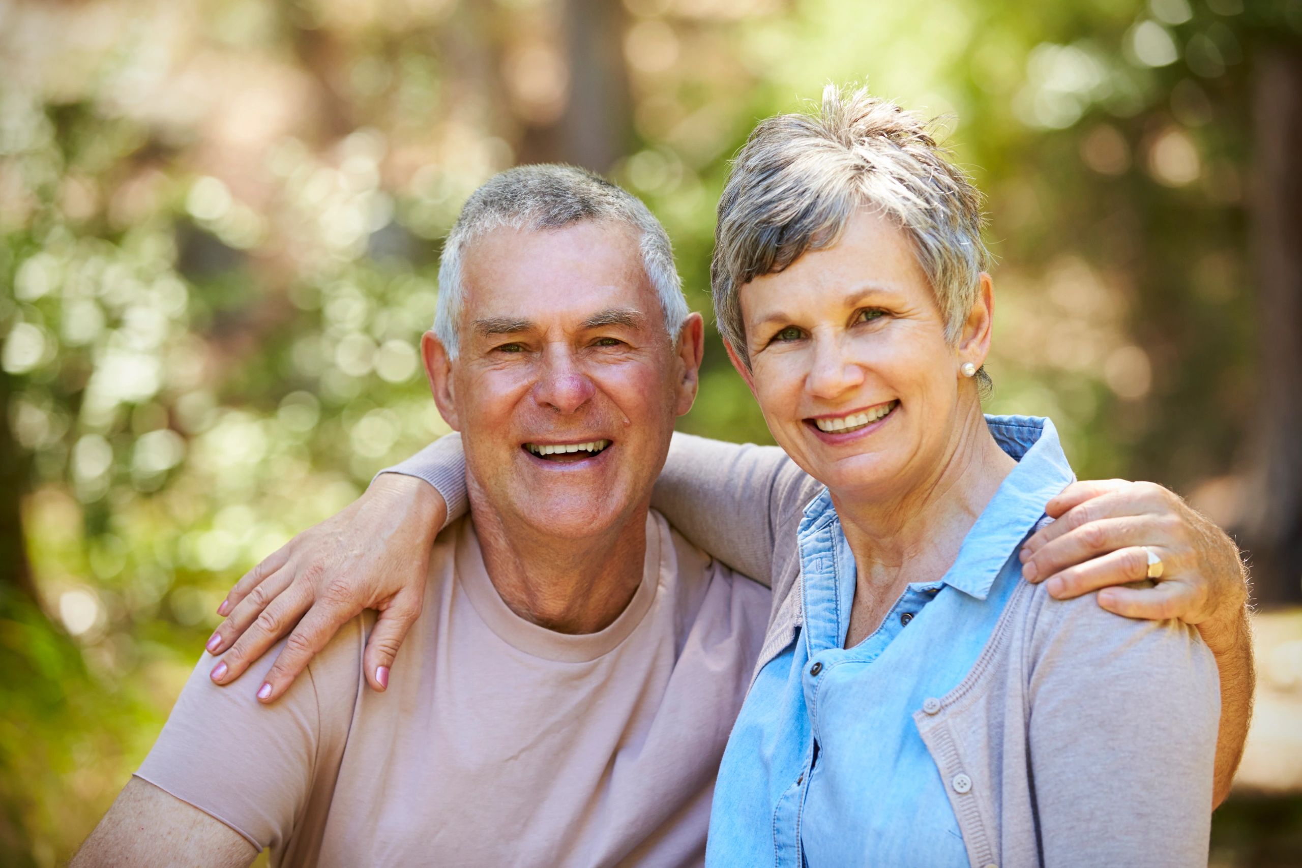 Smiling elderly couple embracing outdoors on a sunny day.