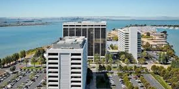 Aerial view of modern office buildings near a waterfront with parking lots and greenery.