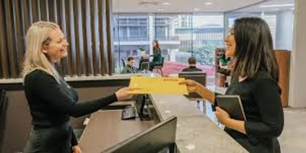 Two women exchanging documents at a modern office reception desk.