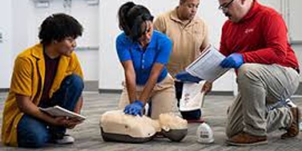 A group practicing CPR on a training mannequin indoors.
