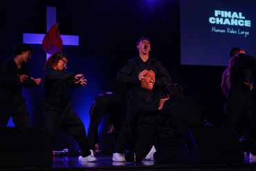 Actors perform a dramatic scene on stage with intense expressions and dark costumes.