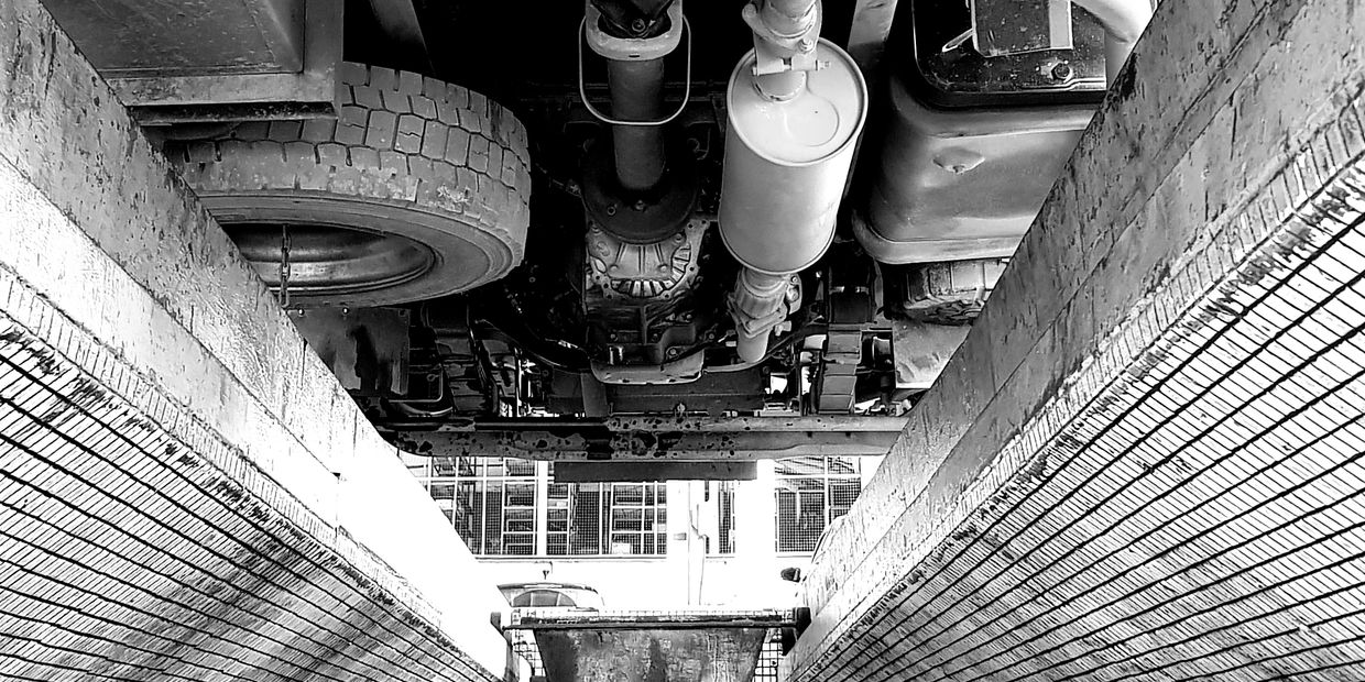 View of a vehicle's undercarriage over a tiled inspection pit in black and white.