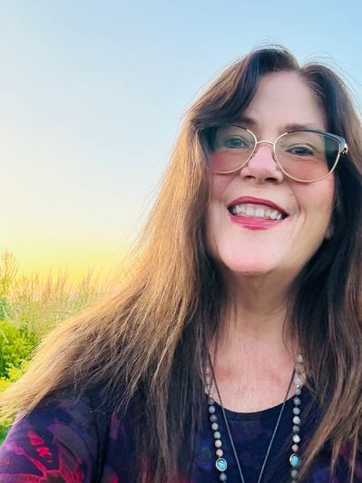 Smiling woman with glasses enjoying an outdoor sunset.