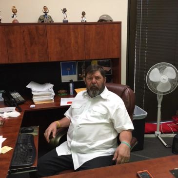Man sitting in an office chair behind a desk.