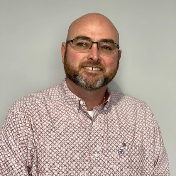 Smiling man with glasses and a beard wearing a patterned shirt.
