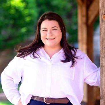 Woman in white shirt smiling outdoors near wooden structure.