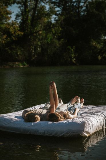 Couple lying on a floating mattress in a lake, holding hands and relaxing.