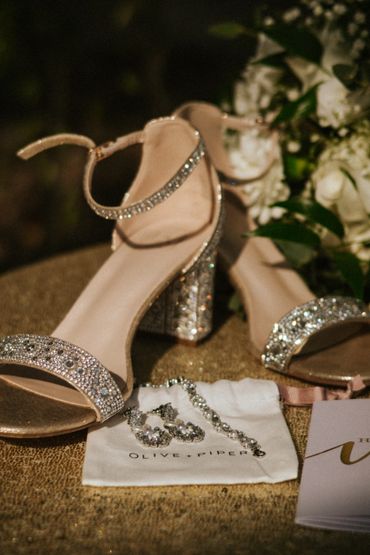 Sparkling bridal heels and jewelry on a golden surface.