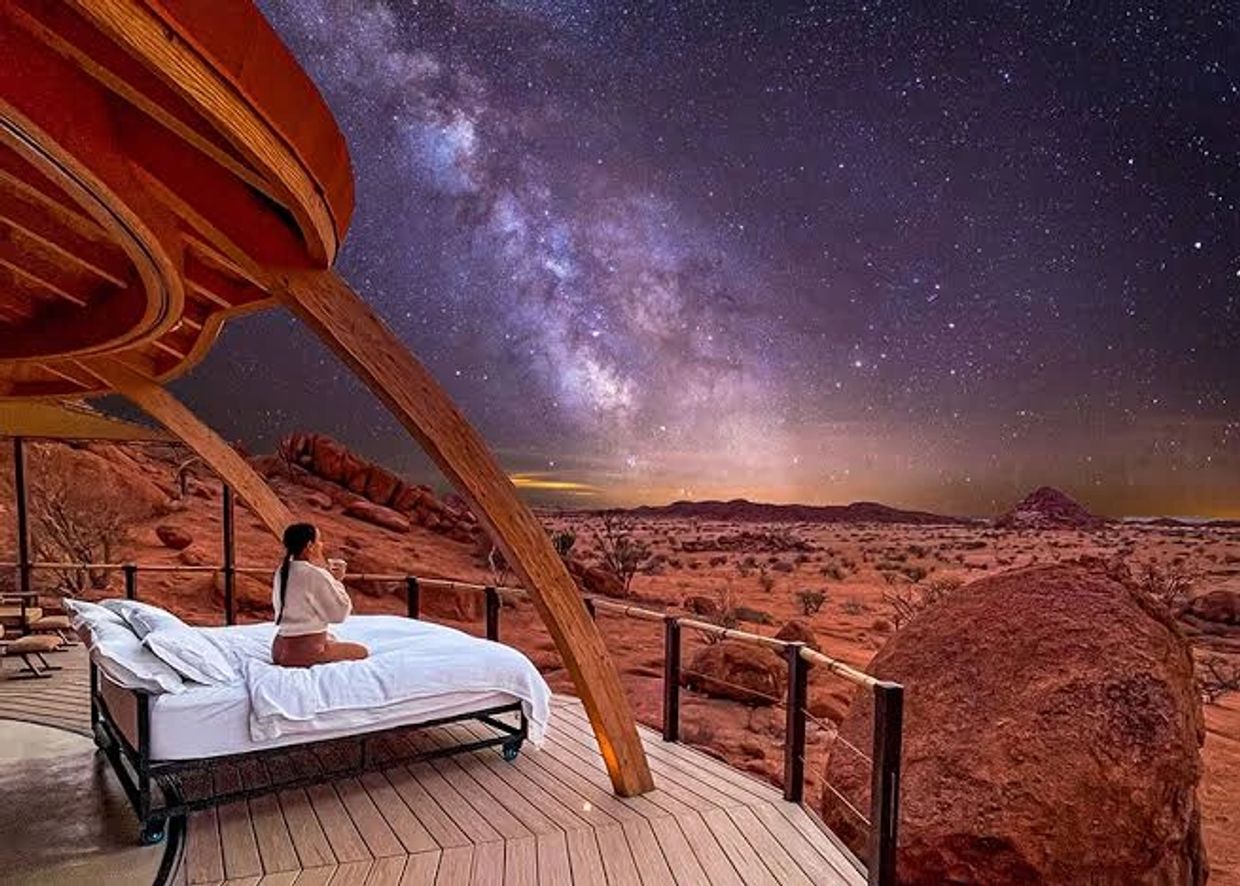 Woman enjoying a starry night and Milky Way view from an outdoor bed in a desert lodge.