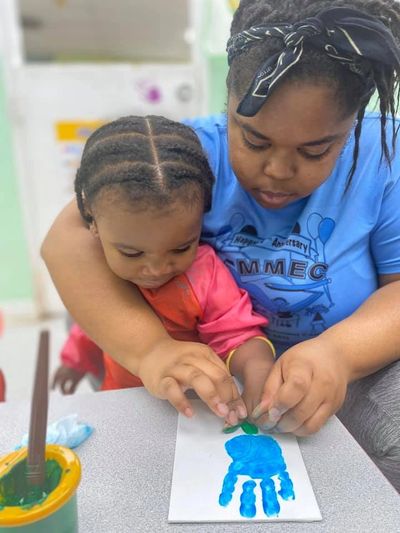 Adult assisting child with hand painting.