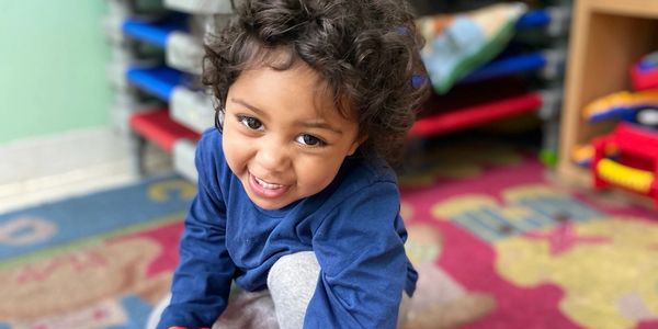 Smiling child playing indoors on colorful carpet.