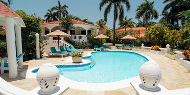 Luxurious villa pool area with palm trees and sun loungers under umbrellas.