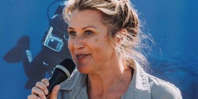 Ten Little Pieces Founder Ali Foley holds a microphone and speaks to a crowd at a beach clean up