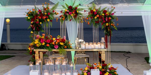 Elegant floral arch and candlelit table set by the ocean at dusk.