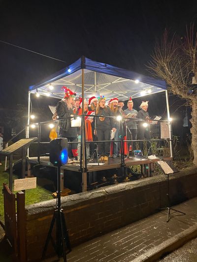 A group singing Christmas carols on a decorated stage at night.