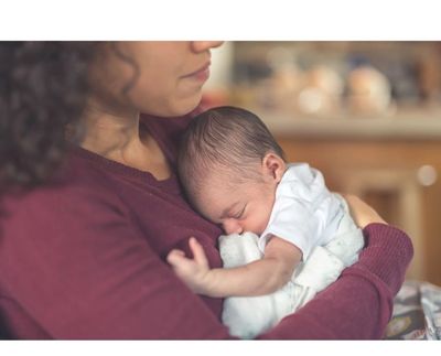 Mother holding a sleeping newborn gently.