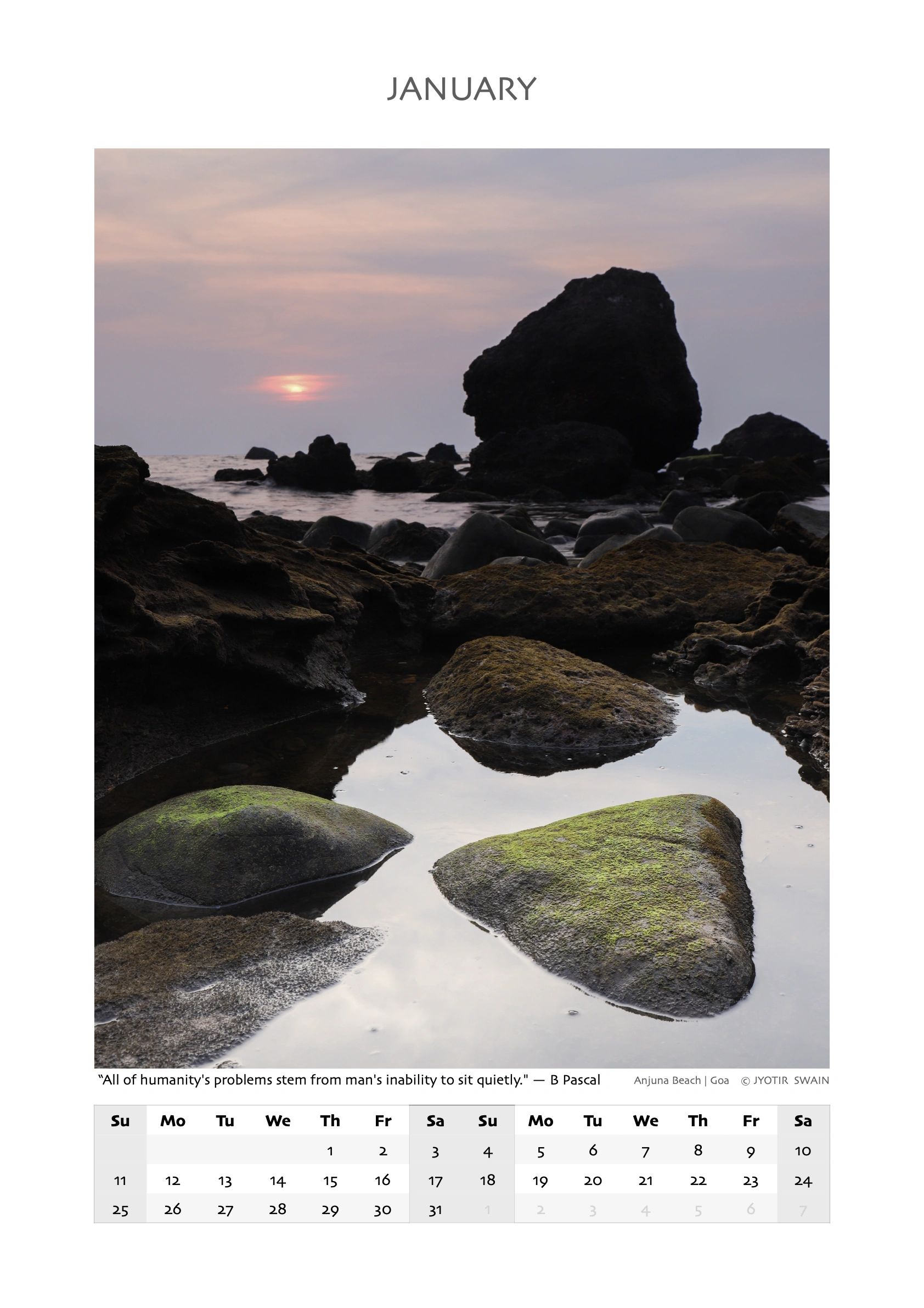 Sunset over moss-covered rocks at Anjuna Beach in Goa during January.