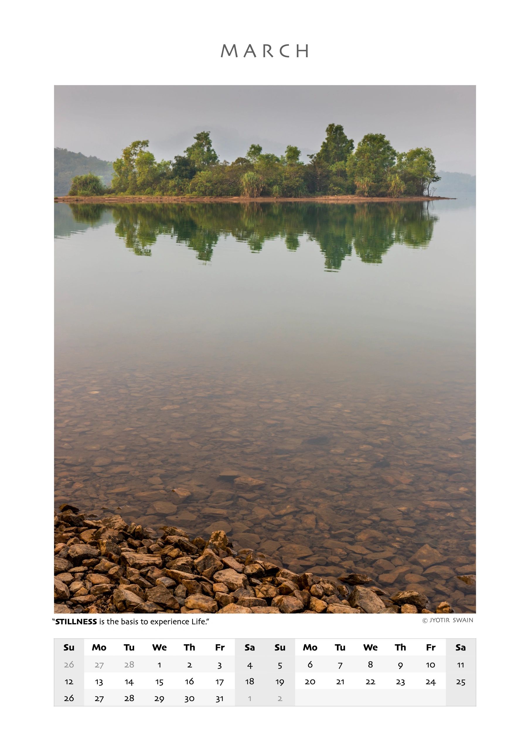 Serene lake with rocky shore and tree reflection for March calendar.