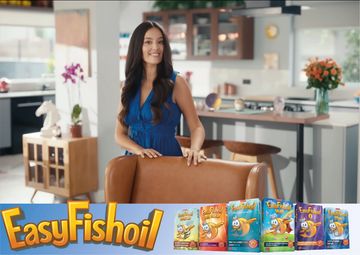 A smiling woman in a blue dress stands behind a chair with EasyFish oil products displayed.