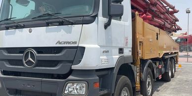 A white Mercedes Actros truck with a large yellow and red machinery attachment.