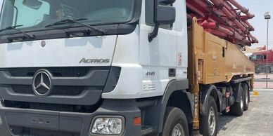 A white Mercedes Actros truck with a large yellow and red machinery attachment.