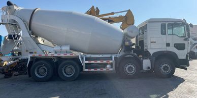 A concrete mixer truck parked on a construction site under clear skies.