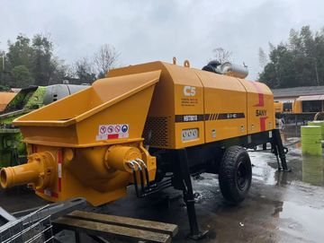 A yellow concrete pump machine parked outdoors on a wet surface.