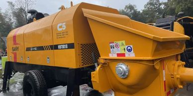 Yellow SANY concrete pump machine parked outdoors on a wet surface.