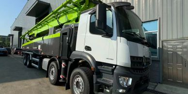 A large white and green construction truck parked beside a building.