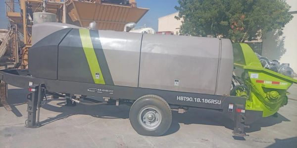 Concrete pump trailer with green and gray design parked outdoors.