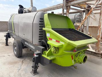 Green and gray concrete pump machine with wheels on a construction site.