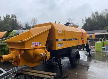 Heavy-duty yellow concrete pump machine on a wet construction site.