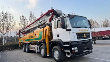 A large concrete pump truck parked outdoors near trees.