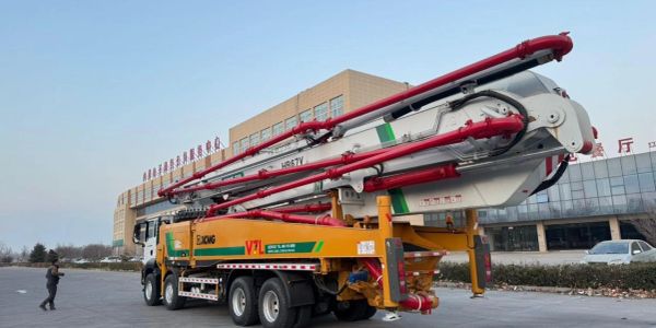Large concrete pump truck parked near a building under clear sky.