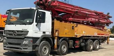 A large Mercedes concrete pump truck with a red boom arm.