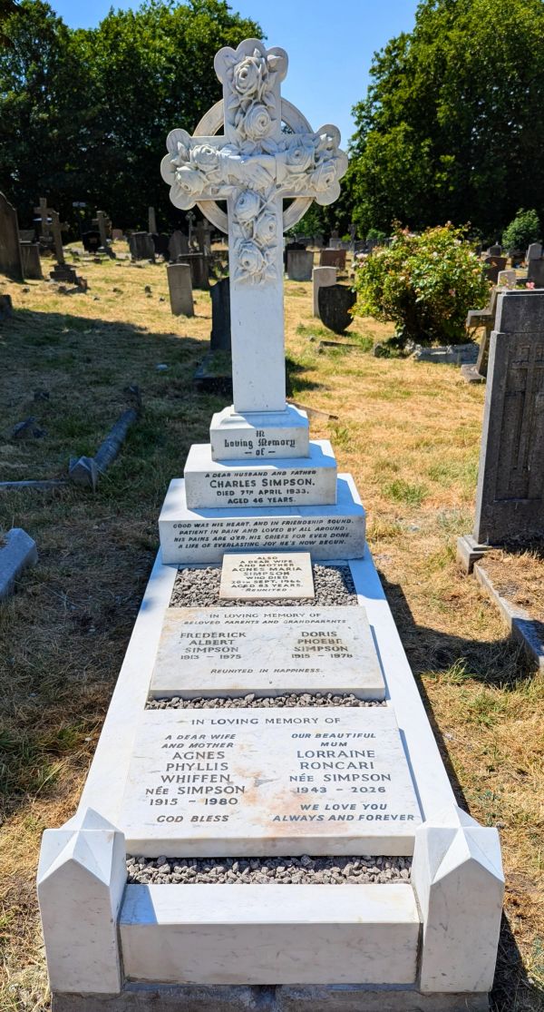 White marble grave in a cemetery with detailed inscriptions and floral cross.