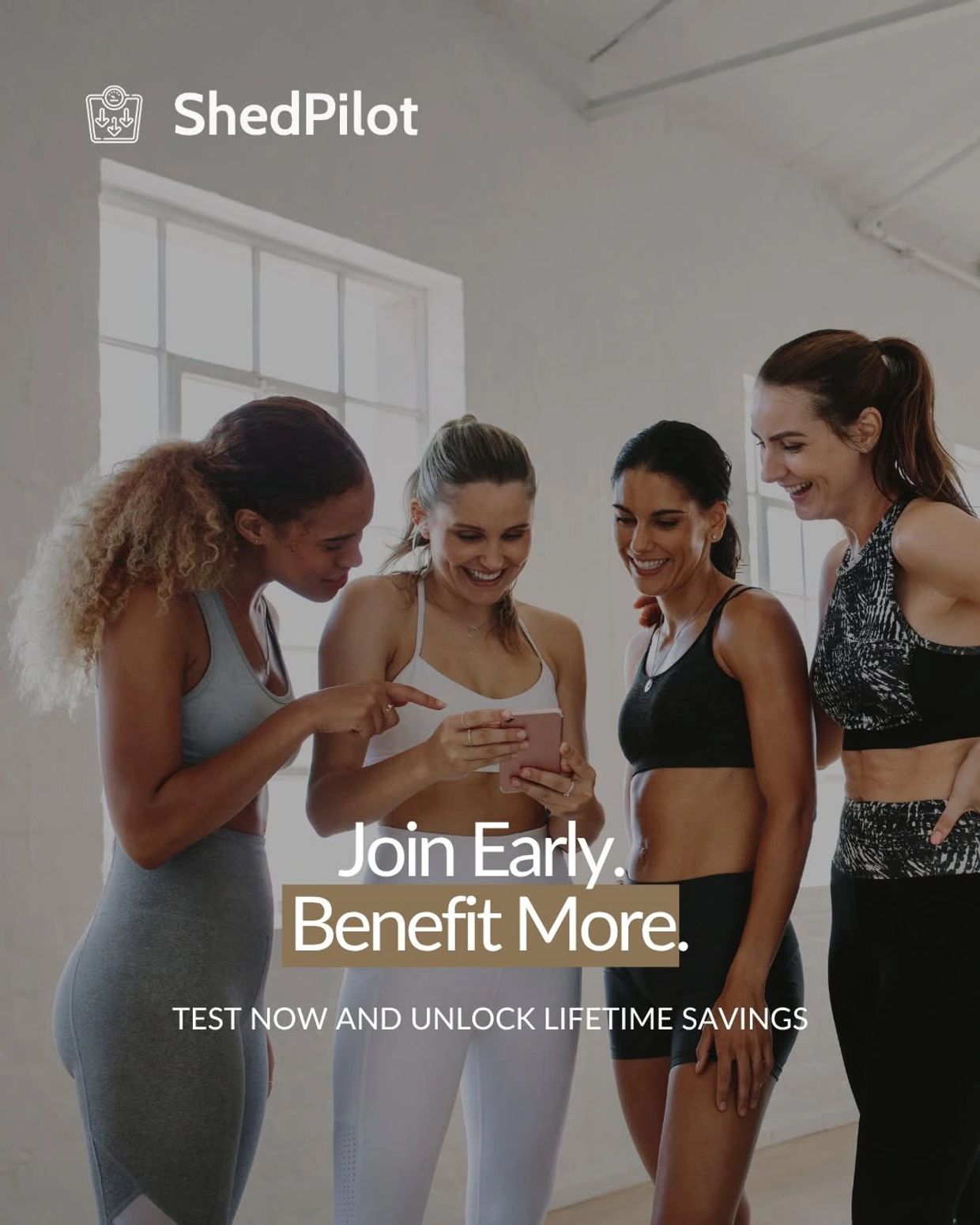 Four women in workout clothes smiling and looking at a phone.