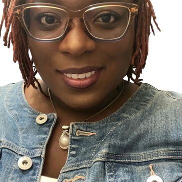 Smiling woman with glasses and a denim jacket.