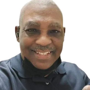 Smiling man wearing a dark polo shirt and a black face mask around his neck.