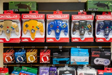 Various colors of N64 controllers and various AC adapters for vintage handheld gaming consoles.