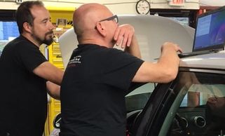 Two men working on a laptop near a car in a garage.