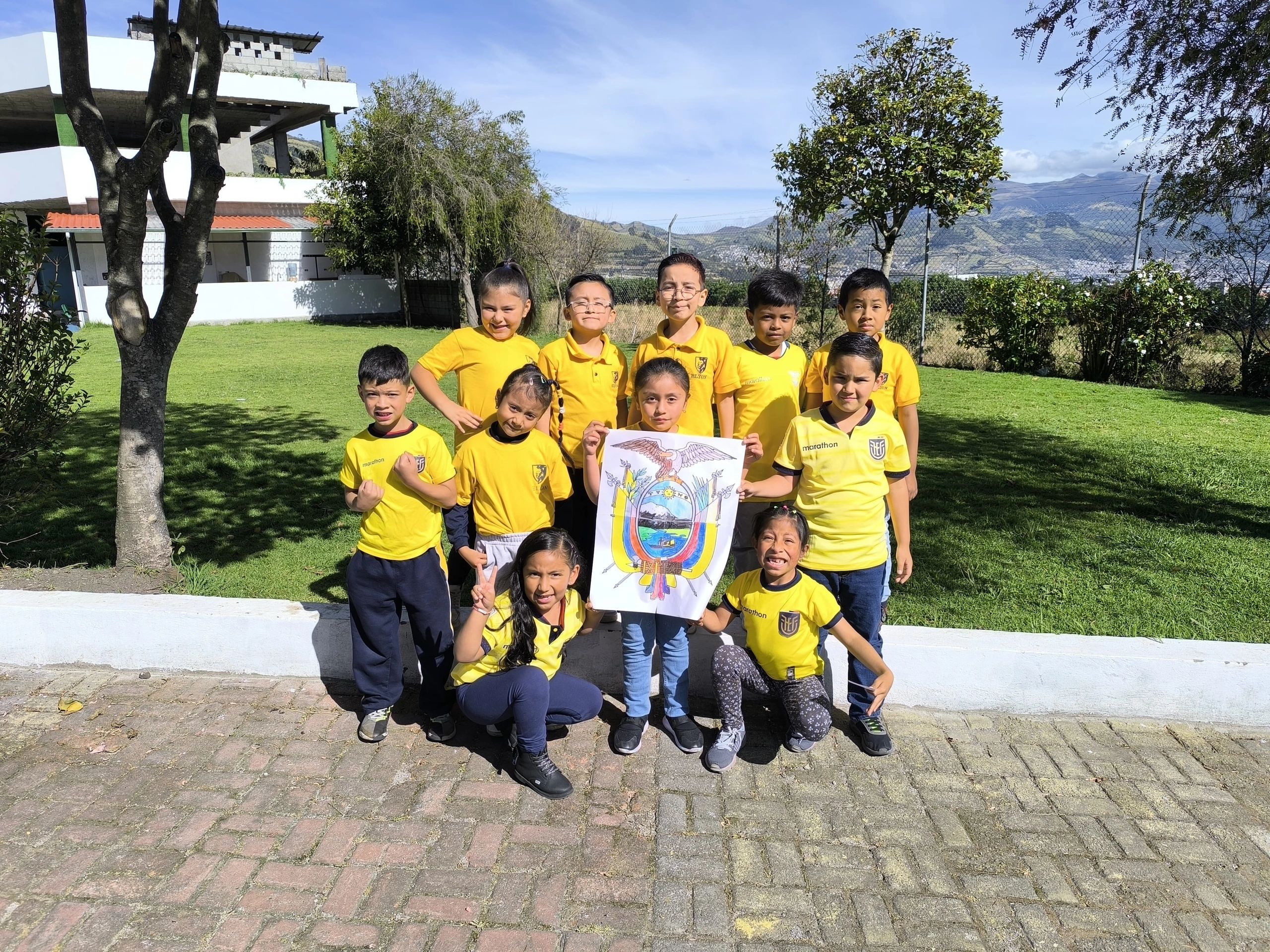 Group of children in yellow shirts holding a colorful drawing outdoors.