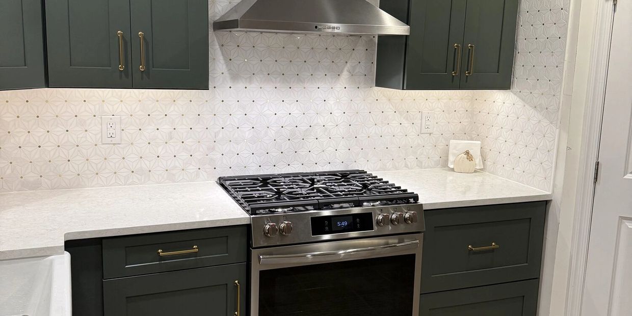 Modern kitchen stove with green cabinets and patterned backsplash.