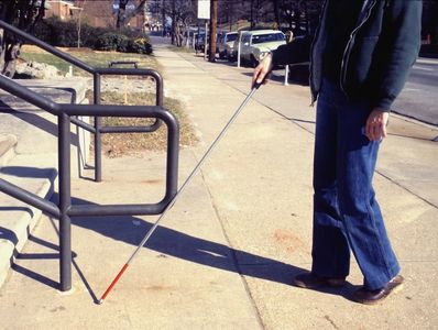 Blind person walking towards the stairs, with the cane to navigate where the stairs & hand rails are