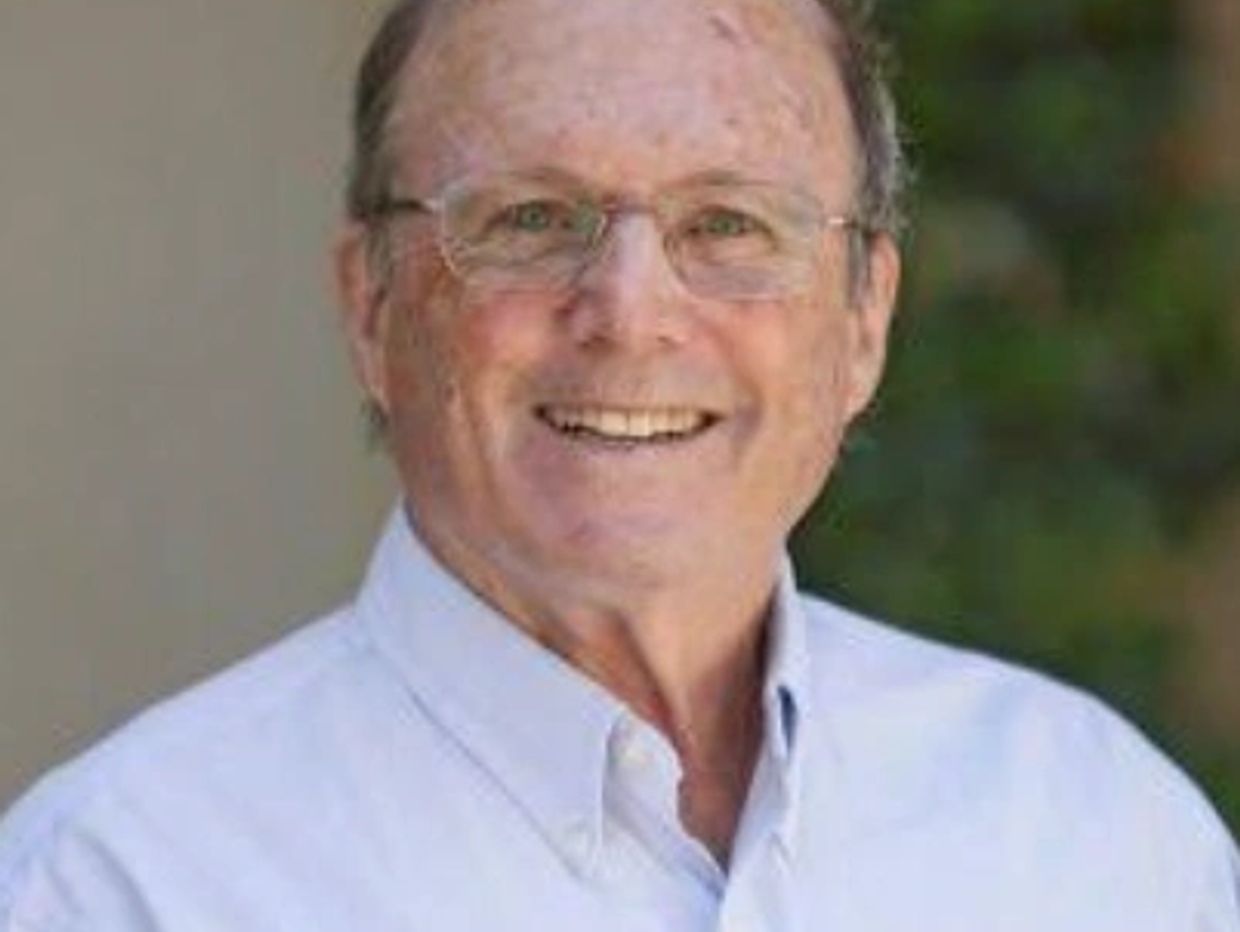 Smiling elderly man wearing glasses and a light blue shirt.